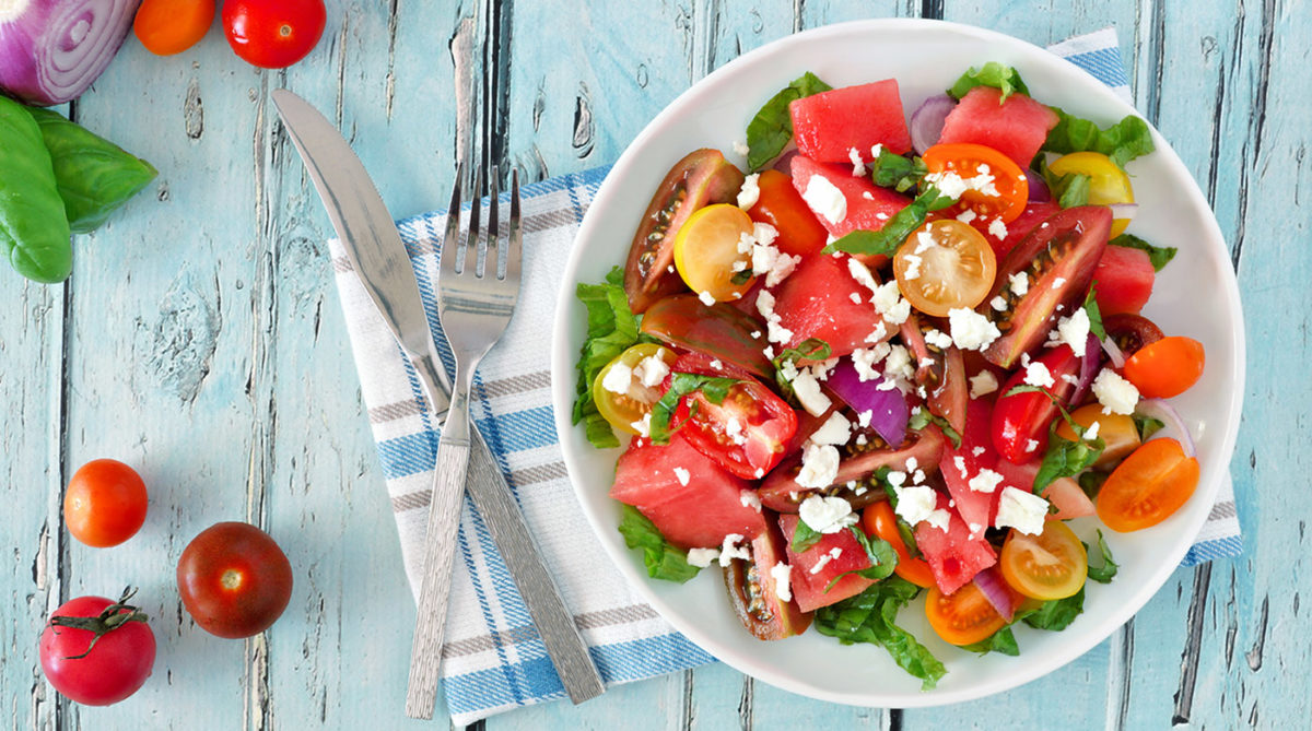 Watermelon and mixed tomato salad with feta cheese, overhead scene on rustic blue wood