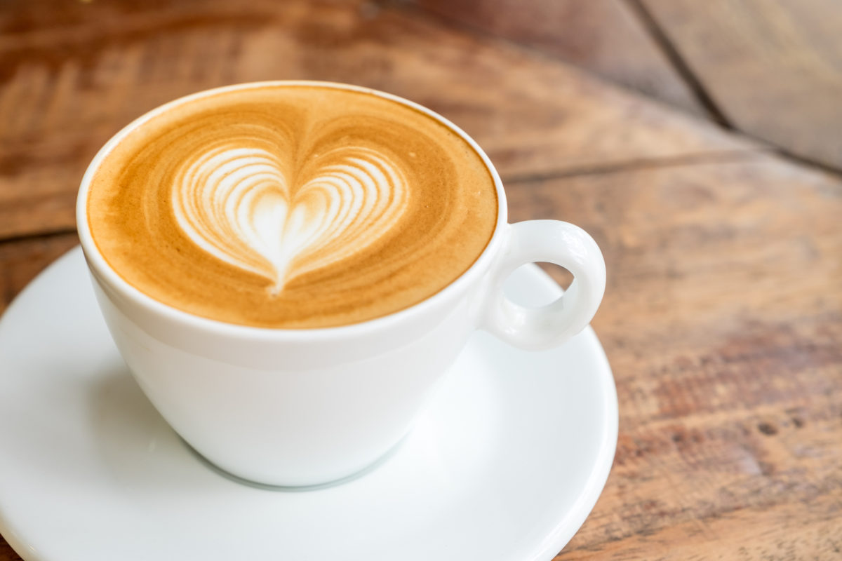 Close up white coffee cup with heart shape latte art on wood table at cafe