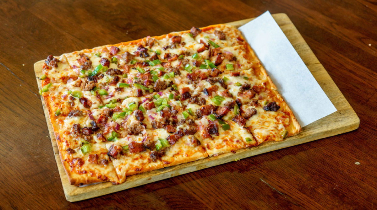 Square pizza with organic ingredients on a wooden board on a restaurant background.